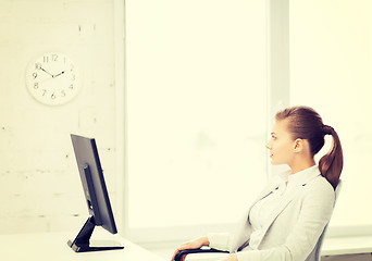 Image showing businesswoman looking at wall clock in office