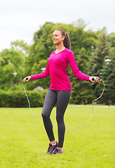 Image showing smiling woman exercising with jump-rope outdoors