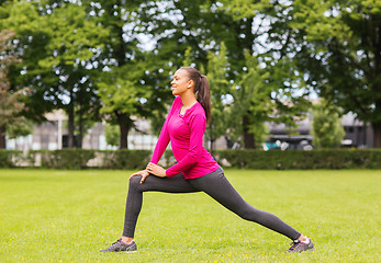 Image showing smiling black woman stretching leg outdoors