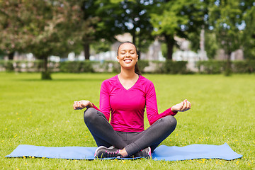 Image showing smiling woman meditating on mat outdoors