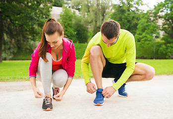 Image showing smiling couple tying shoelaces outdoors