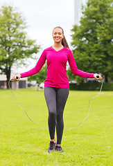 Image showing smiling woman exercising with jump-rope outdoors