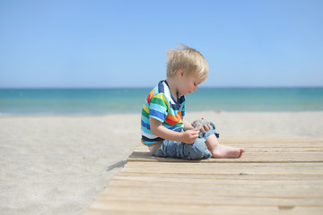 Image showing Boy sitting on a wooden walkway on the beach