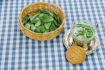 Image showing mint tea in cup and cookie on checkered tablecloth 