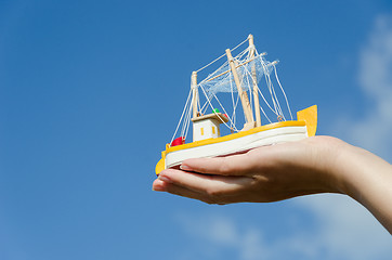 Image showing wooden ship toy on palm on blue sky background 