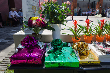 Image showing gift in glossy paper and bouquets on table outdoor 