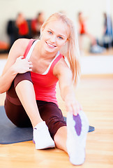 Image showing smiling woman stretching on mat in the gym