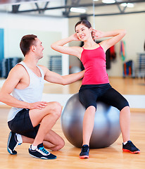 Image showing male trainer with woman doing crunches on the ball