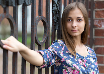 Image showing Portrait of a beautiful girl near the old rusty wrought fence