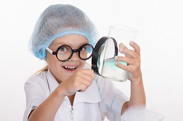 Image showing Girl chemist examines flask under a magnifying glass