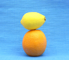 Image showing A lemon lying upon an orange on a  blue background