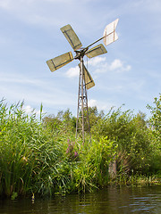 Image showing Small and rusted old metal windmill at the waterside