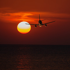 Image showing Passenger plane flying at a low altitude at sunset and the sun b