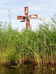 Image showing Small and rusted old metal windmill at the waterside