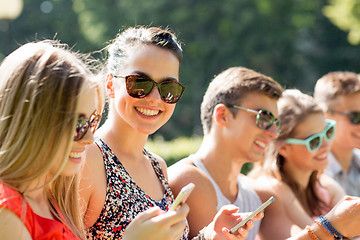 Image showing smiling friends with smartphones sitting in park