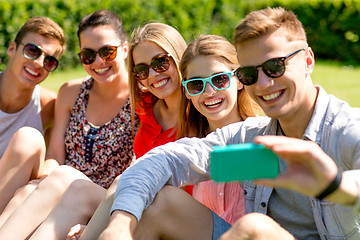 Image showing smiling friends with smartphone sitting on grass