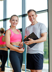 Image showing smiling young woman with personal trainer in gym