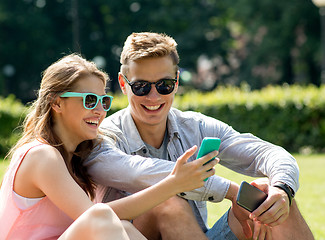 Image showing smiling friends with smartphones sitting in park