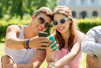 Image showing smiling friends with smartphones sitting in park