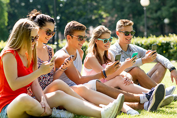 Image showing smiling friends with smartphones sitting on grass