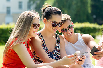 Image showing smiling friends with smartphones sitting in park