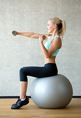 Image showing smiling woman with dumbbells and exercise ball