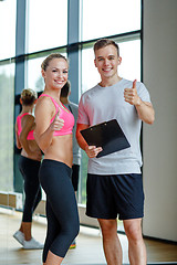 Image showing smiling young woman with personal trainer in gym