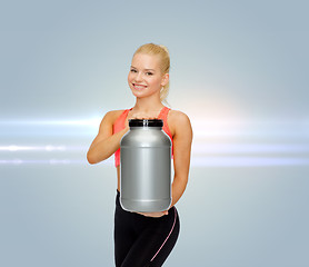 Image showing smiling sporty woman with jar of protein