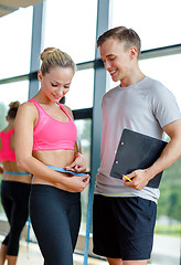 Image showing smiling young woman with personal trainer in gym