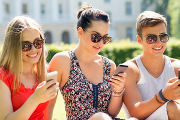 Image showing smiling friends with smartphones sitting on grass