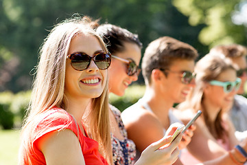 Image showing smiling friends with smartphones sitting in park