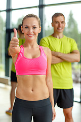 Image showing smiling man and woman showing thumbs up in gym