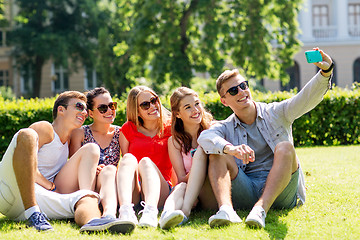 Image showing smiling friends with smartphone sitting on grass