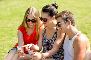 Image showing smiling friends with smartphones sitting in park