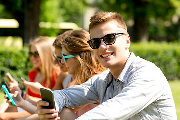 Image showing smiling friends with smartphones sitting in park