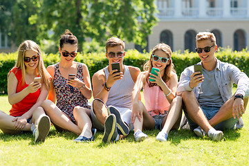 Image showing smiling friends with smartphones sitting on grass