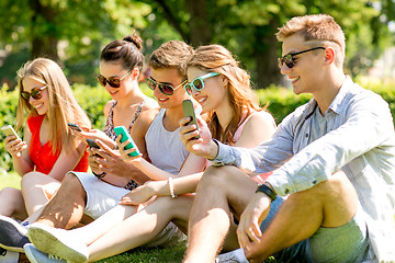 Image showing smiling friends with smartphones sitting on grass