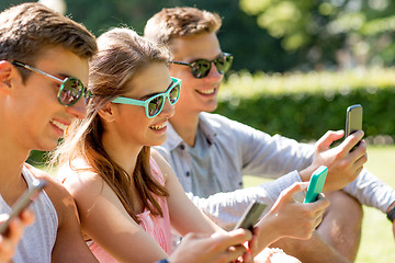 Image showing smiling friends with smartphones sitting on grass