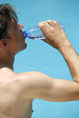 Image showing Attractive man drinks water at the swimming pool