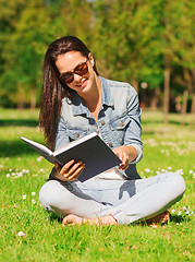 Image showing smiling young girl with book sitting in park