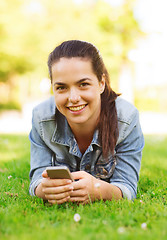 Image showing smiling young girl with smartphone lying on grass