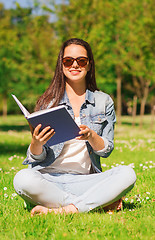 Image showing smiling young girl with book sitting in park