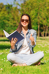 Image showing smiling young girl with book sitting on grass