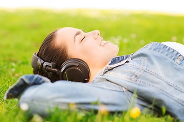 Image showing smiling young girl in headphones lying on grass