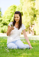 Image showing smiling young girl with smartphone sitting in park