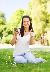 Image showing smiling young girl with smartphone sitting in park