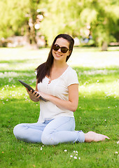 Image showing smiling young girl with tablet pc sitting on grass