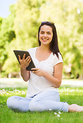 Image showing smiling young girl with tablet pc sitting on grass