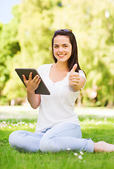 Image showing smiling young girl with tablet pc sitting on grass