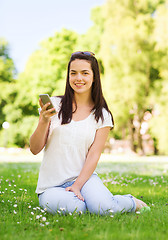 Image showing smiling young girl with smartphone sitting in park